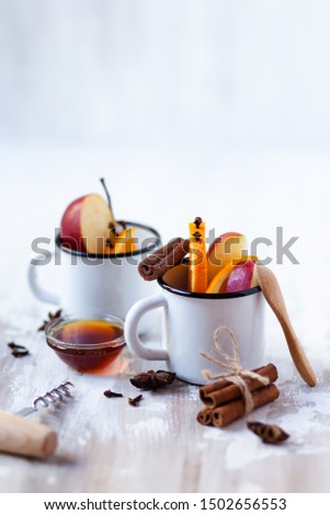Two white metal mugs with ingredients for hot mulled wine - traditional christmas beverage. Ripe apple and orange, spices, honey. Corkscrew for wine bottle. Holiday festive mood. Copy space for text