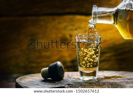 Glass of golden rum, with bottle. Bottle pouring alcohol into a small glass. Brazilian export type drink Royalty-Free Stock Photo #1502657612