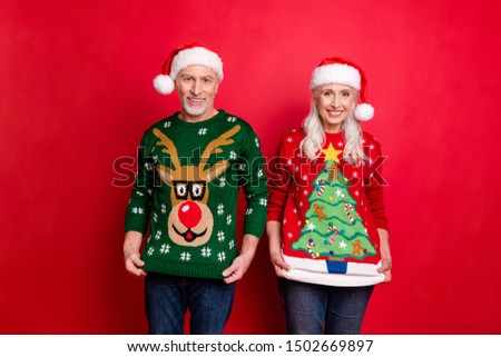 Ugly pullover party concept. Two cheerful friendly excited positive elderly grey white haired grandmother grandfather in caps showing comic retro pictures on pullovers isolated background