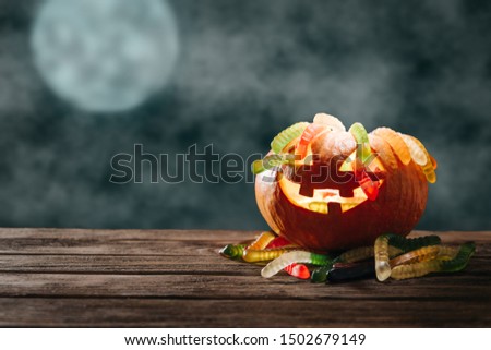 Glowing carved pumpkin with colorful candies in form of worms on wooden table in Halloween night.