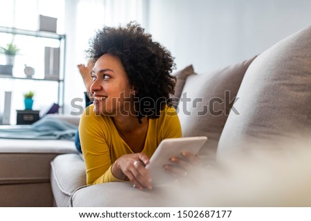 Social media time. Staying in touch with her tablet. Cheerful woman sitting on couch using tablet pc at home in the living room. Smiling young woman with tablet on the sofa Royalty-Free Stock Photo #1502687177