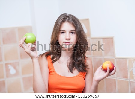 Pretty teen girl holding a peach and a fresh green apple in her hands, indoor.Beautiful teenage girl holding fruits and looking at the camera.Picture of beautiful teenage 