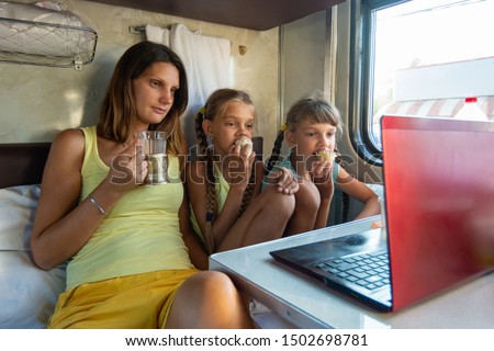 Mom drinks tea, children eat ice cream on a train, look at a laptop together