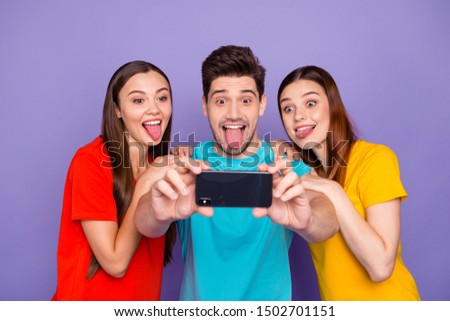Portrait of three nice attractive lovely charming crazy childish cheerful cheery glad guys wearing colorful t-shirts taking making selfie having fun isolated over violet lilac background