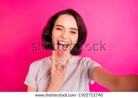 Self portrait of beautiful charming cute cheerful nice attractive millennial rock fan girl getting her tongue out showing her fingers horned taking selfie fuchsia pink vibrant color background