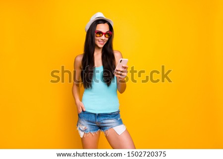 Photo of cheerful cute funky confident charming attractive youngster millennial looking into smartphone browsing wearing teal tank-top jeans denim shorts cap hat isolated vivid color background