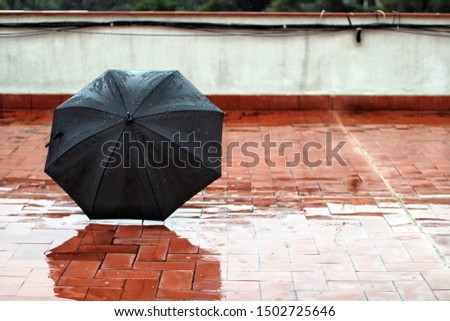Black umbrella on the wet orange floor during a rainy day. Copy Space.