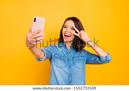 Portrait of cheerful positive girl photographer take selfie with cell phone on journey vacation make v-signs have fun feel funny funky wear denim jeans shirt isolated over yellow color background