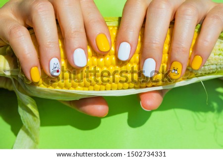 Yellow  manicure  design  on female hand with yellow fruits closeup on corn in the background.