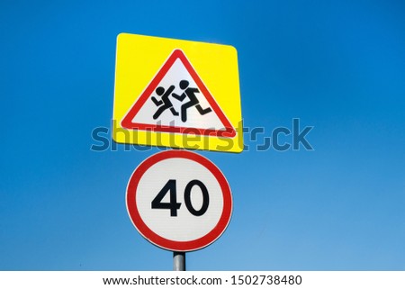 International signs 'Speed limit' (to 40 km/hour, below) & 'Children crossing' (above). Clear blue sky is on background