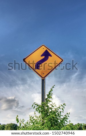 Curve ahead sign with weeds and blue sky