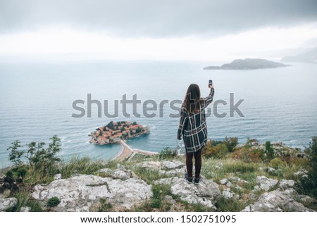 A girl tourist or a blogger takes a selfie or takes photos or videos of a beautiful view in Montenegro.