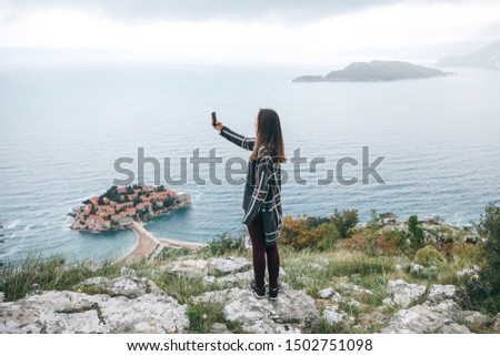 A girl tourist or a blogger takes a selfie or takes photos or videos of a beautiful view in Montenegro.