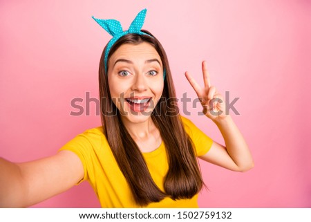 Close up photo of cheerful lady with blue headband making v-signs wearing yellow t-shirt isolated over pink background