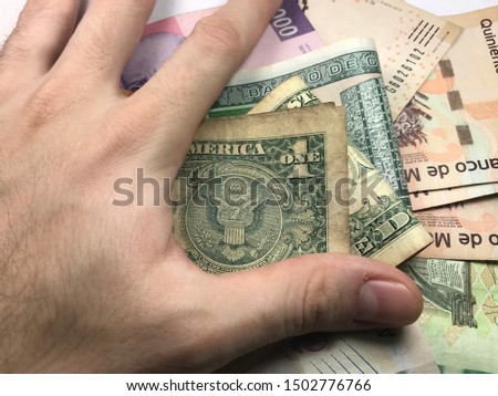 Many mexican pesos bills spread randomly over a flat surface with a hand over them