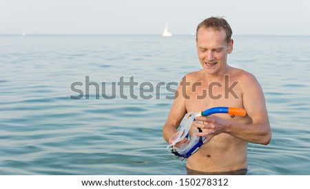 Man standing in the sea with a goggles and snorkel in his hand as he prepares to put them on to go out snorkeling and exploring