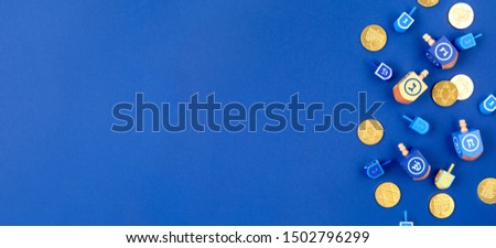 Dark blue background with multicolor dreidels and chocolate coins. Hanukkah and judaic holiday concept. Horizontal, banner format style