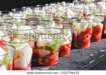 Slices of fruits: watermelon, melon and green grape in a glass, to-go fresh healthy vegetarian food; many cups on the table Royalty-Free Stock Photo #1502796650