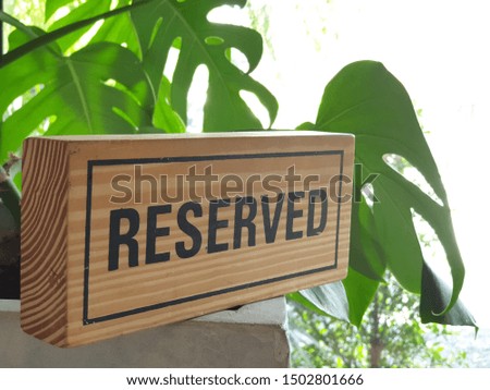 Wooden sign reserved on a white table. The back is decorated with trees.  Reserved sign on a table in restaurant for family dinners.