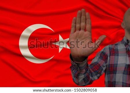 male hand with a gesture of protest, oaths against the backdrop of a silk national flag, the concept of denial and prohibition and prohibition, close-up, copy space