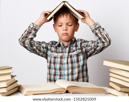 Tired school boy doing homework at desk over white background. Tired boy reading book while sitting at table, close-up.