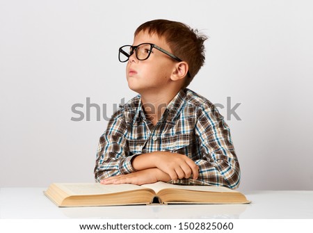 Boy at desk bored tired stressed of reading books. Close up portrait of a school boy sitting at table with pile of books over white background with copy space.