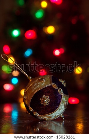 A sparkling decorative x-mas ornament with tree lights in the background.