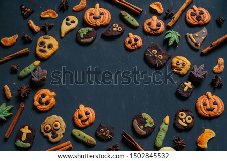 Scary pumpkin face, jack o lantern, Pumpkin shape cookies, Halloween cookies jack o lantern, skeleton, ghost, witch and cinnamon sticks spices decoration in dark background, copy space