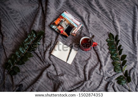 Notebook with pen, red cup of tea and photos on the gray plaid. Flat lay with notebook, pen, green leaves and printed photos.