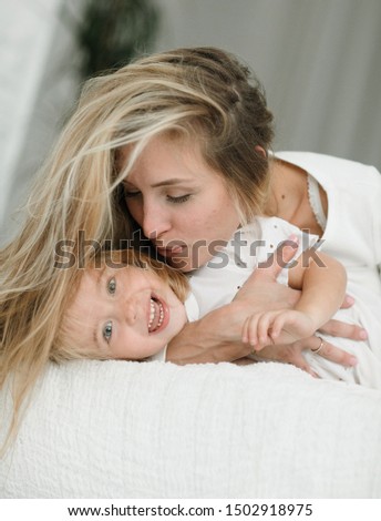 A friendly and loving family is resting. Emotional portrait of a happy and positive young mother hugging her funny and smiling little daughter lying on the bed. Motherhood. Happy childhood. Summer