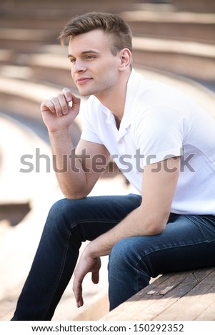 Thoughtful young man. Side view of thoughtful young man sitting outdoors and looking away