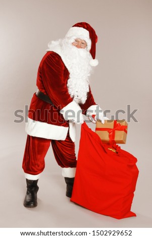 Authentic Santa Claus with sack and gift on grey background