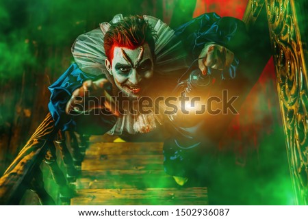 A portrait of an angry crazy clown from a horror film with a lantern on the stairs. Halloween, carnival.
