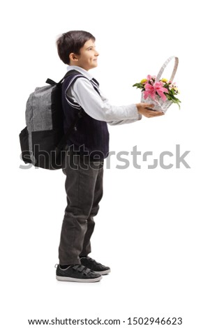 Full length profile shot of a schoolboy in a uniform holding a basket of flowers isolated on white background
