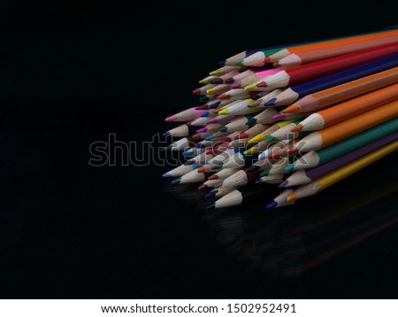A lot of multi-colored pencils, on a black background. A pile of colored pencils on the table. Concept: start life with a blank sheet of paper. Life is beautiful and diverse with different colors.