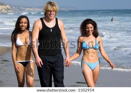 A man and two young women strolling down the beach laughing and having fun
