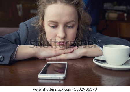 Disappointed sad woman looking at phone and waiting message or call Royalty-Free Stock Photo #1502986370