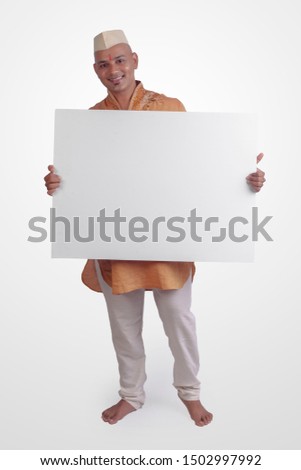 Bald man holding a white blank sign board standing over white background in traditional Indian Kurta Pyjamas with Ghandi Topi (Cap).