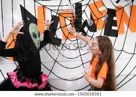 Girl kids dress up as Halloween Alien mask costume on head for playing with pumpkin toy on Halloween day in living room at home