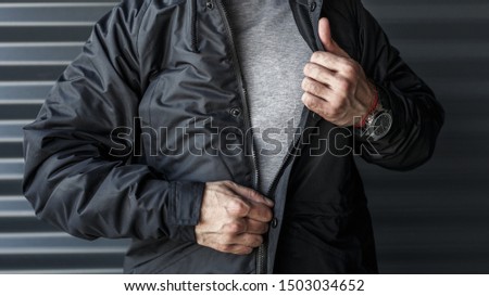 A man in a black jacket is standing against the wall. Street photo. Urban. Wear. Logo