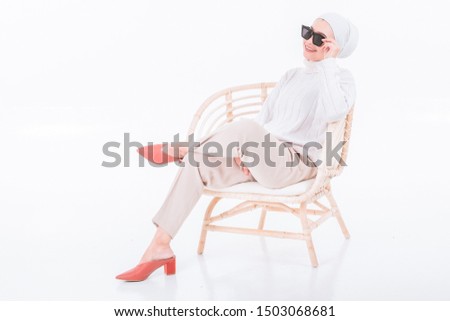 A beautiful Malay girl wearing white shirt and white hijab with sunglasses in various pose while seating on the wooden chair. isolated white background. copy space 