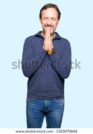 Middle age handsome man wearing a sweater praying with hands together asking for forgiveness smiling confident.