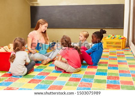 Group of children and teacher reading a fairytale book in the day-care center