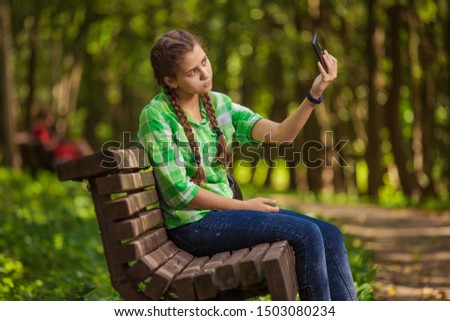 Emotional girl teenager with long hair hairstyle braids in a green shirt sitting on a bench in the park.