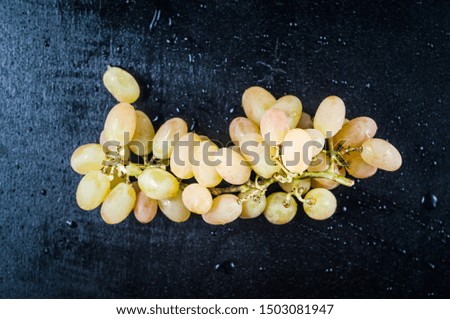 A bunch of homemade white grapes on a black background in drops of water.