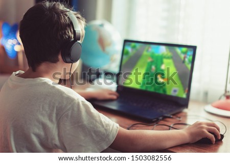 Little dependent gamer boy playing on laptop at home Royalty-Free Stock Photo #1503082556