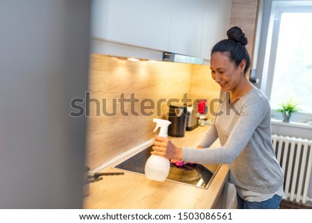 Woman cleaning house. Beautiful mature Asian housewife polishing oven in the kitchen. Woman doing housework, cleaning the kitchen. Woman with bottle of spray cleanser cleaning oven at home kitchen