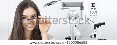 concept of eye examination, woman patient smiling with spectacles isolated in optician office with diagnostic tools on white background, prevention and control eyesight Royalty-Free Stock Photo #1503086582