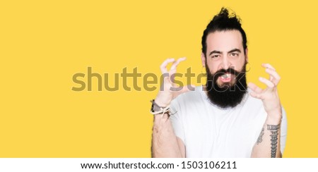 Young hipster man with long hair and beard wearing casual white t-shirt Shouting frustrated with rage, hands trying to strangle, yelling mad