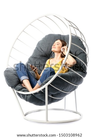 Young woman listening to music while relaxing in armchair against white background